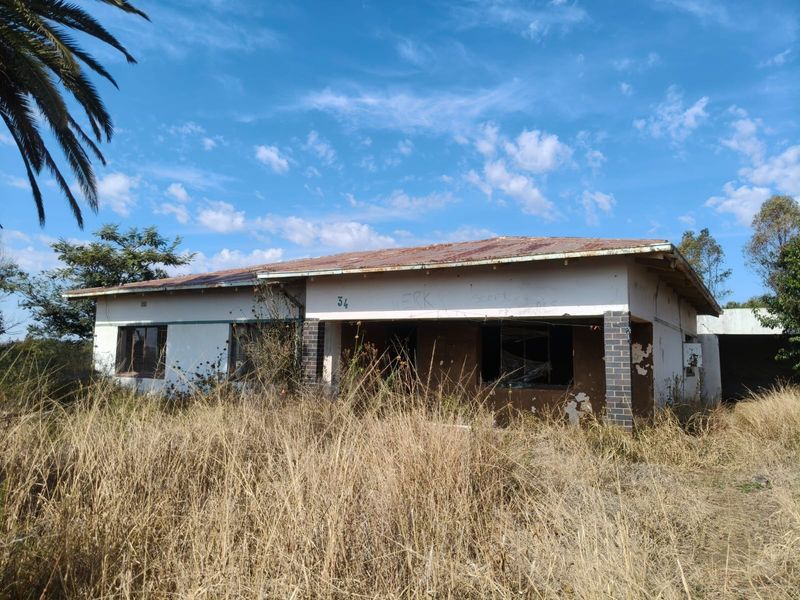 A single-story house in need of significant renovation, featuring a rusted metal roof and overgrown grounds, presenting a major restoration opportunity.