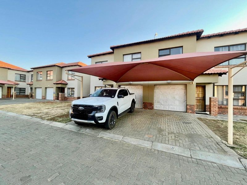Front exterior view of a townhouse featuring a paved driveway, a shade sail carport, and double garage doors.