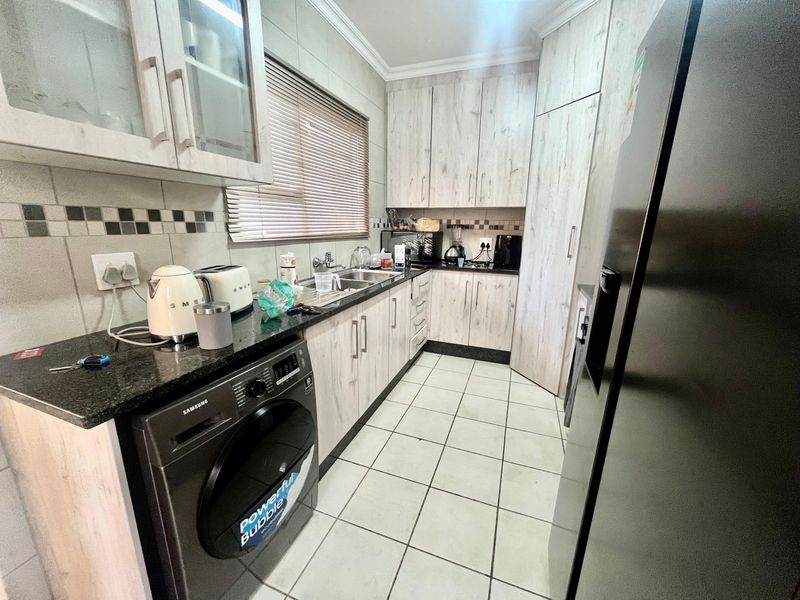 A functional kitchen featuring light wood-grain cabinetry, granite countertops, a double basin sink, and tiled flooring with space for a washing machine.