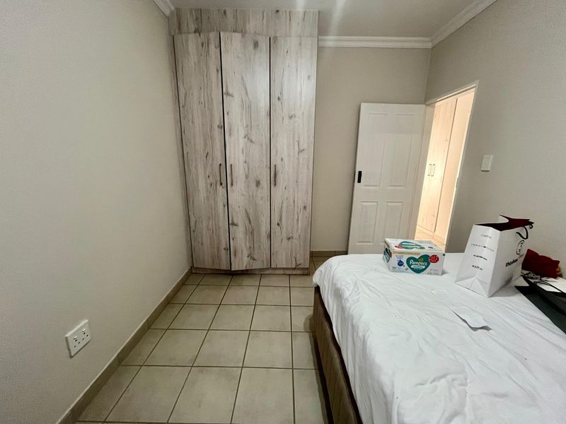 A bedroom featuring built-in cupboards with a wood-look finish and neutral tiled flooring.