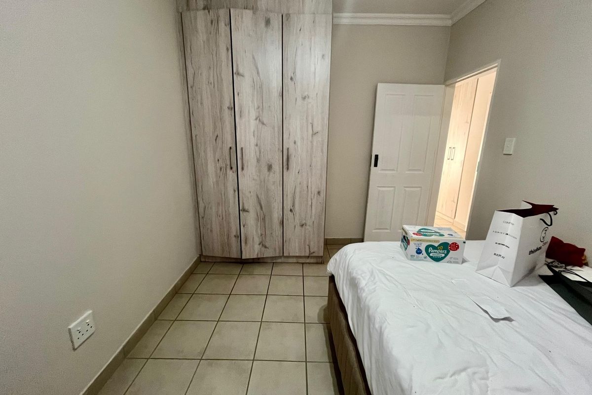 A bedroom featuring built-in cupboards with a wood-look finish and neutral tiled flooring.
