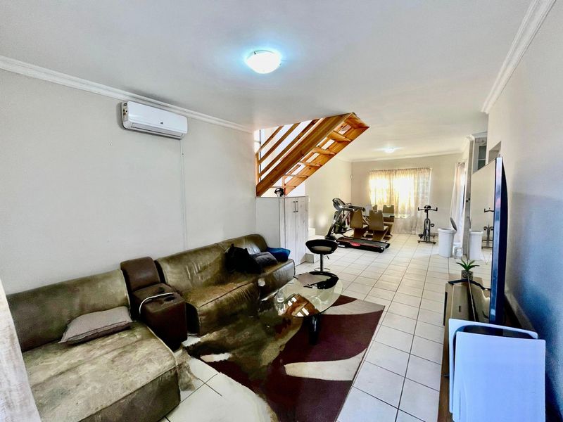 Open-plan living area featuring tiled flooring, a wooden staircase, and a wall-mounted air conditioning unit.