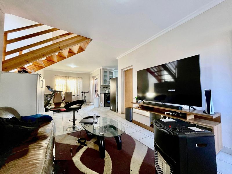 Open-plan living area featuring tiled flooring, a wooden staircase, and an integrated kitchen space, offering a functional layout for modern townhouse living.
