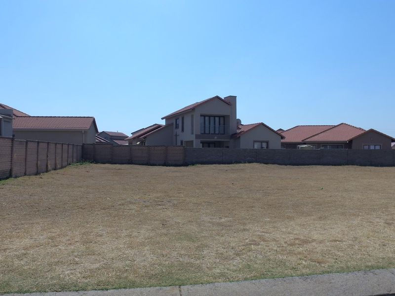 A vacant residential plot of land enclosed by a perimeter brick wall, situated in a developed suburban neighborhood.
