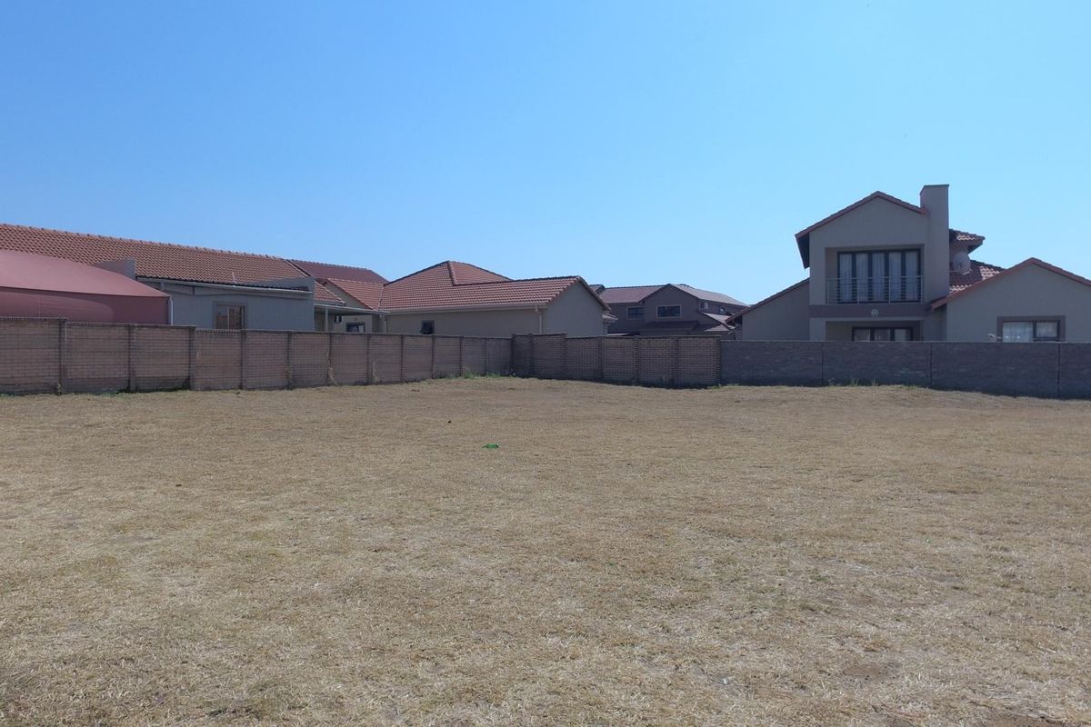 A vacant residential plot featuring a level grass surface enclosed by a perimeter brick wall, situated within a developed residential estate.
