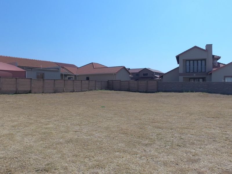 A vacant residential plot featuring a level grass surface enclosed by a perimeter brick wall, situated within a developed residential estate.