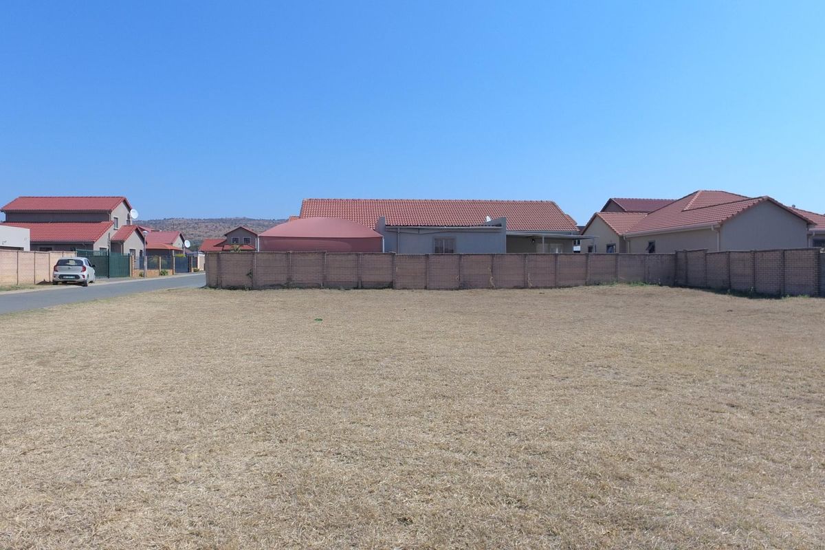 A vacant residential plot of land featuring a level grass surface, enclosed by a perimeter brick boundary wall in a suburban neighborhood setting.