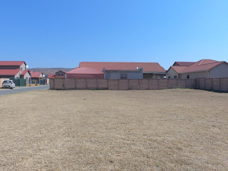 A vacant residential plot of land featuring a level grass surface, enclosed by a perimeter brick boundary wall in a suburban neighborhood setting.