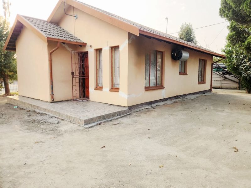 Exterior view of a single-story house featuring a tiled roof, security gate, and external geyser, with visible plaster work around the window frames.