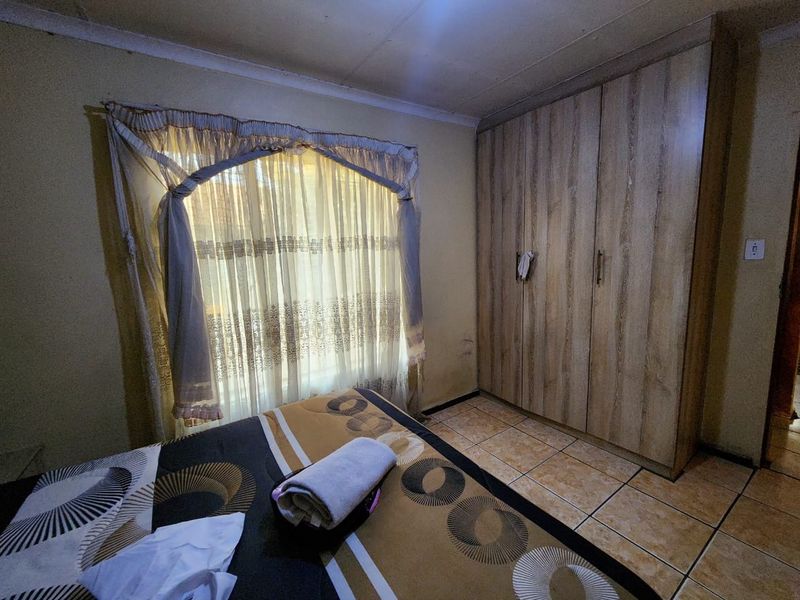 A bedroom featuring tiled flooring and a built-in wooden wardrobe, requiring cosmetic updates to the wall finishes.