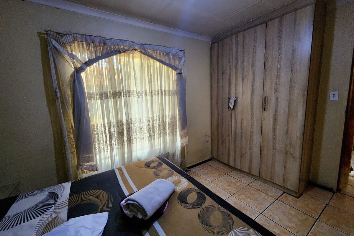 A bedroom featuring tiled flooring and a built-in wooden wardrobe, requiring cosmetic updates to the wall finishes.