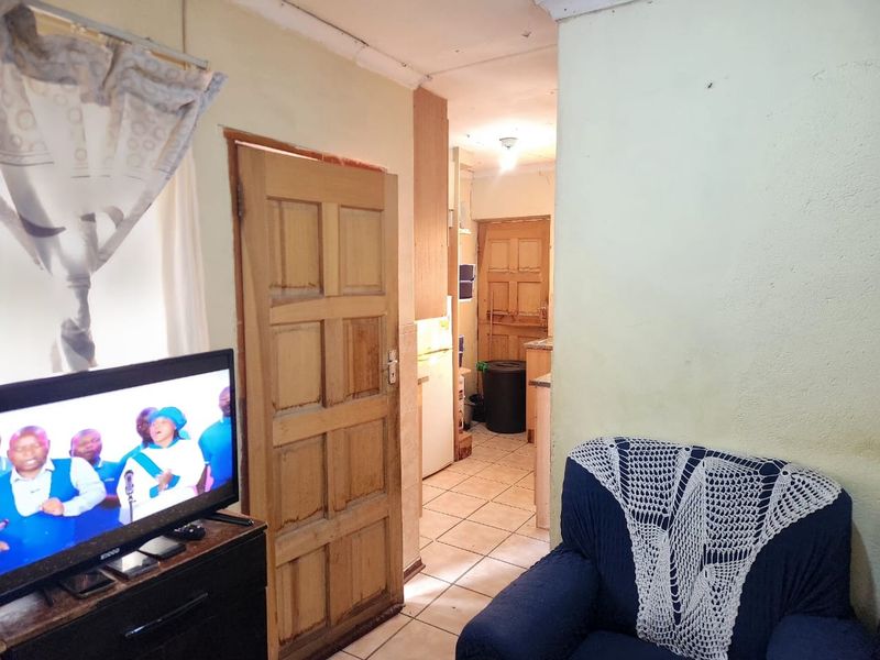 A living area featuring tiled flooring and a timber panel door, leading through to a secondary space. The room requires cosmetic updates to wall finishes.