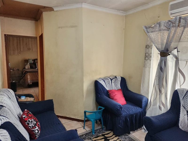 A living room area featuring tiled flooring and a wall-mounted air conditioning unit, showing signs of wear and requiring cosmetic updates.