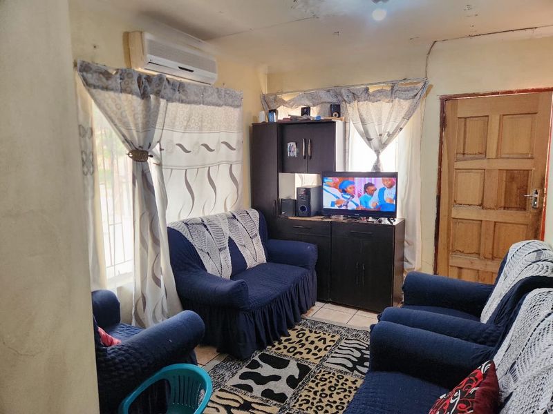 A living room featuring tiled flooring, a wall-mounted air conditioning unit, and a timber panel door, showing signs of wear on the ceiling and walls.