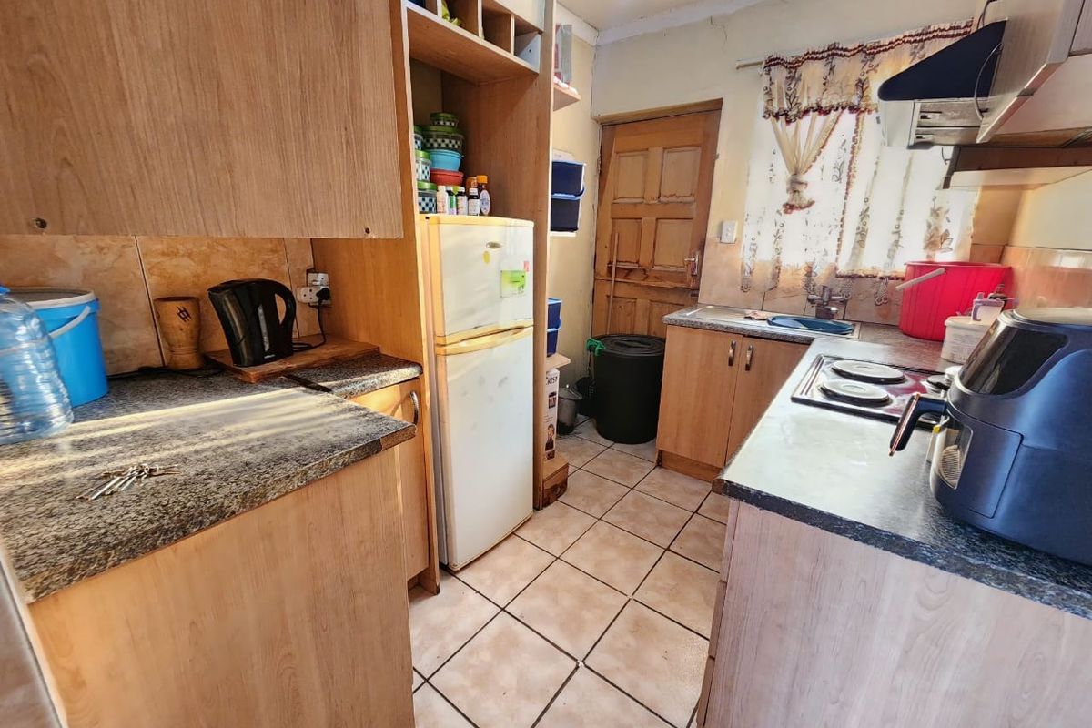 A compact kitchen featuring laminate cabinetry, granite countertops, and ceramic tile flooring, requiring some maintenance and cosmetic updates to modernize the space.