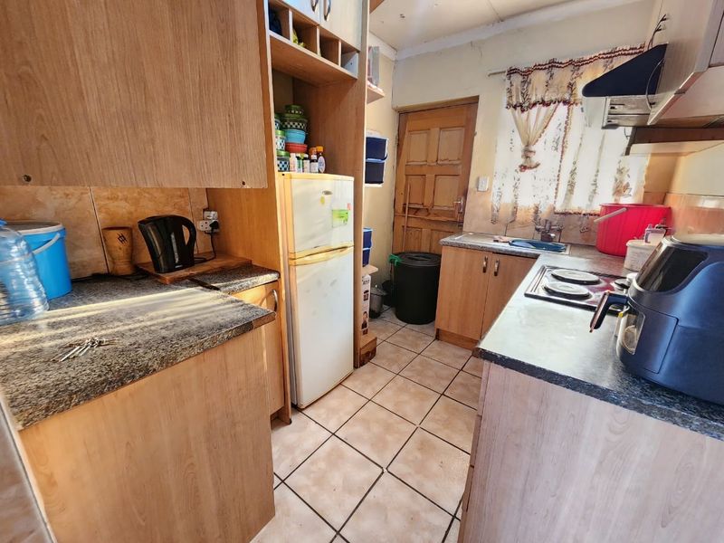 A compact kitchen featuring laminate cabinetry, granite countertops, and ceramic tile flooring, requiring some maintenance and cosmetic updates to modernize the space.
