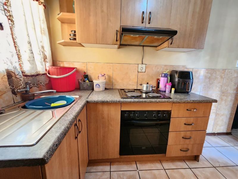 A functional kitchen featuring laminate cabinetry, a built-in oven with hob, extractor fan, and tiled finishes throughout.