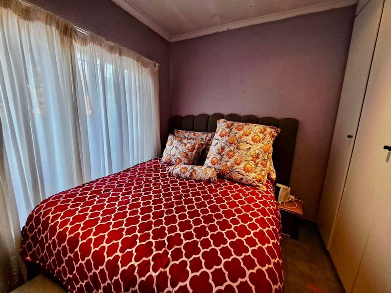 A compact bedroom featuring a built-in wardrobe and large window with curtain rails, requiring cosmetic updates to the wall finishes.