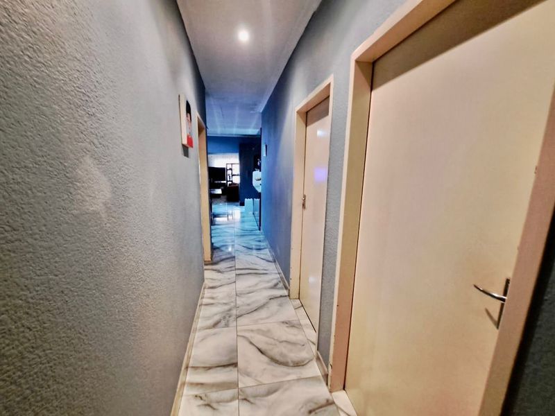 A narrow interior hallway featuring marble-effect tiled flooring, recessed ceiling lighting, and multiple internal doors leading to adjacent rooms.