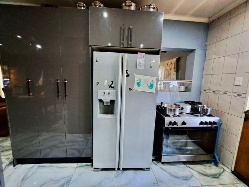 A functional kitchen featuring modern grey high-gloss cabinetry, a stainless steel gas stove with oven, and tiled flooring.