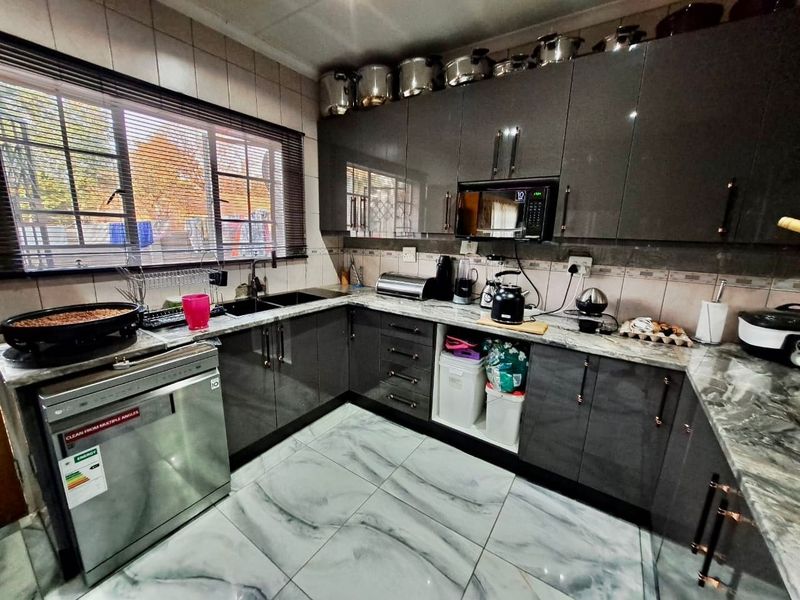 Modern kitchen featuring high-gloss grey cabinetry, marble-effect floor tiles, stone-look countertops, and integrated appliances including a built-in microwave and dishwasher.