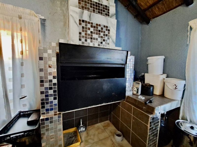 Covered patio area featuring a built-in braai with decorative mosaic tiling and a rustic thatched roof structure.
