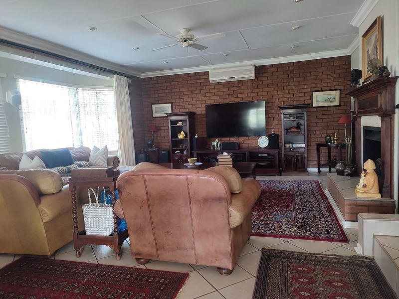 Spacious living room featuring an exposed brick feature wall, a traditional fireplace with a wooden mantel, tiled flooring, and integrated air conditioning.