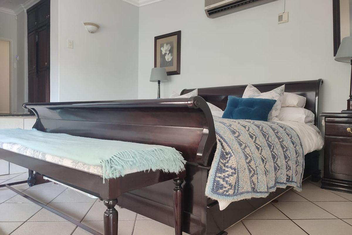 A spacious bedroom featuring tiled flooring, built-in cupboards, and a wall-mounted air conditioning unit.