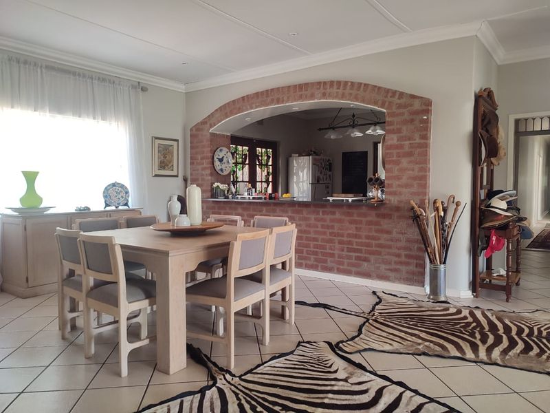 Open plan dining area featuring a distinctive exposed brick archway connecting to the kitchen, complemented by neutral tiled flooring and coved ceilings.