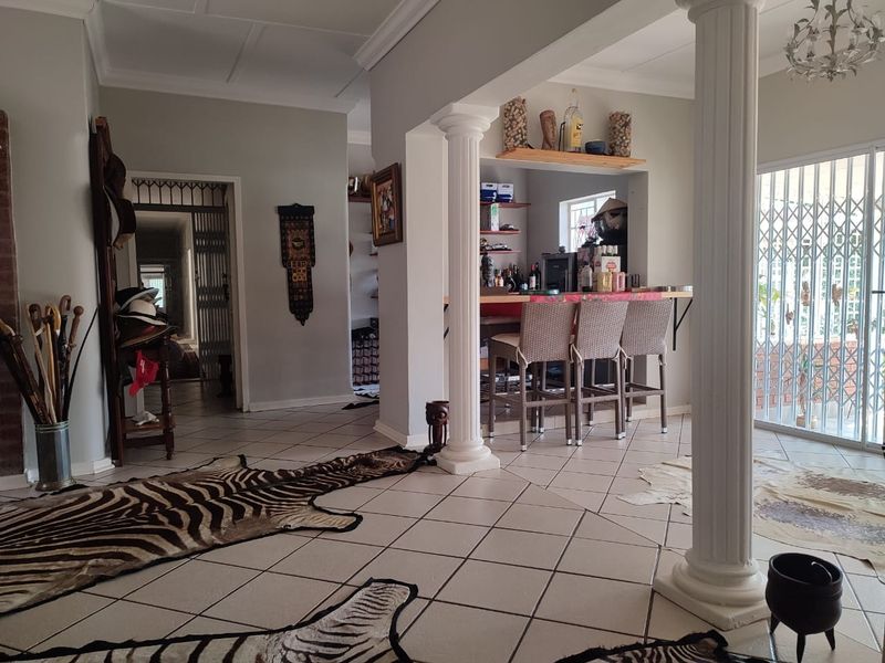 Open plan living area featuring ceramic floor tiles, decorative columns, and a built-in bar counter, leading to a secure patio area.