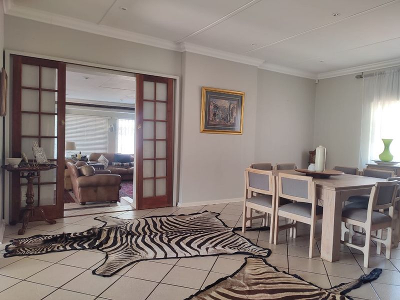 A bright dining room featuring tiled flooring, coved cornicing, and wooden sliding doors that provide access to an adjacent living area.