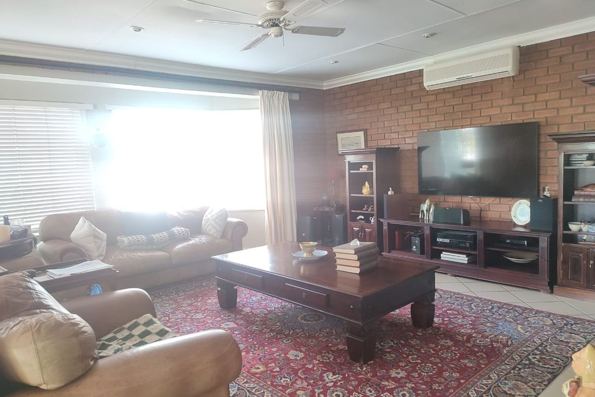 Spacious living room featuring an exposed brick feature wall, tiled flooring, ceiling fan, and wall-mounted air conditioning unit.