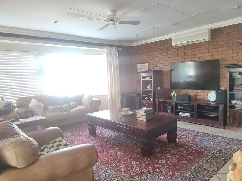 Spacious living room featuring an exposed brick feature wall, tiled flooring, ceiling fan, and wall-mounted air conditioning unit.