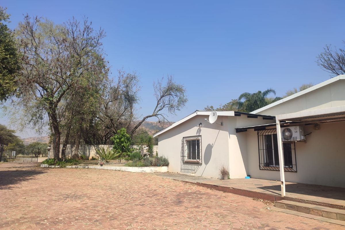 Rear exterior view of the farm property featuring a paved driveway, covered patio area, and security-fitted windows.