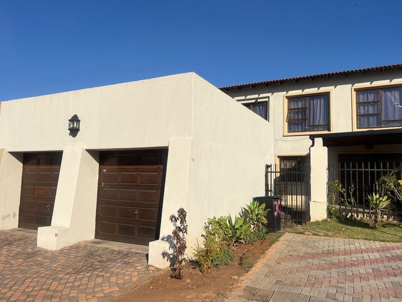 Front elevation of a townhouse featuring a double garage, paved driveway, and secure gated entrance with established garden beds.