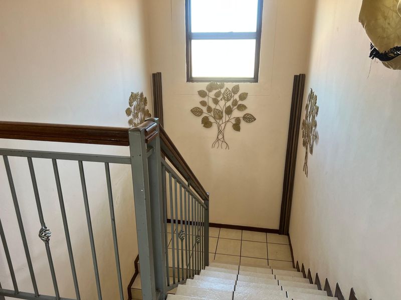 A staircase hallway featuring a metal railing with a wooden handrail, tiled steps, and a window providing natural light.