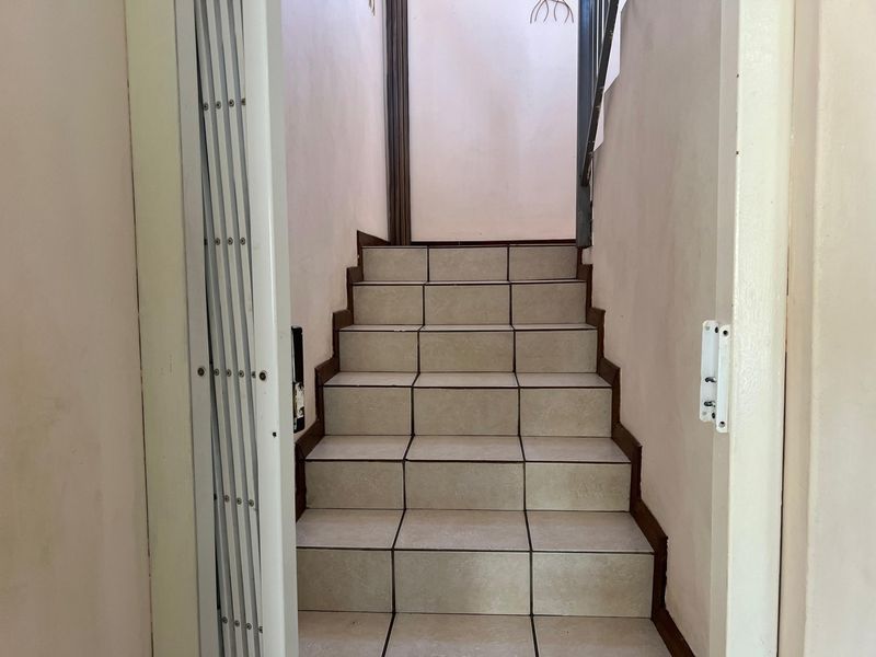 A functional staircase featuring tiled steps, a security gate, and a metal handrail, providing access between levels in the townhouse.