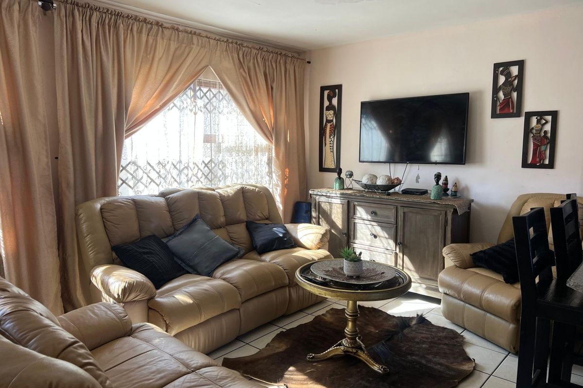 A living room featuring tiled flooring and a security gate on the window, with a visible water stain on the ceiling.
