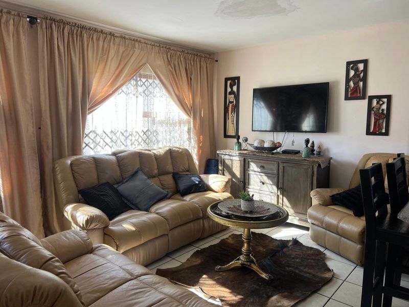 A living room featuring tiled flooring and a security gate on the window, with a visible water stain on the ceiling.