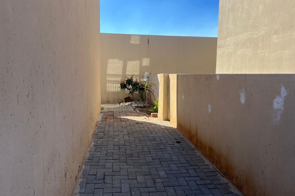 A narrow paved side passage or rear courtyard area enclosed by high boundary walls, requiring minor maintenance and cosmetic finishing.