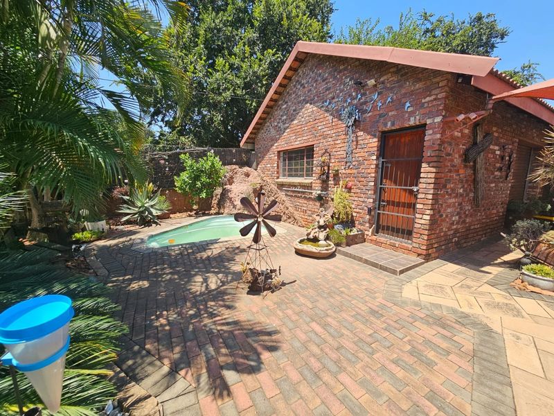 Outdoor pool area featuring a brick-clad building, paved patio space, and established garden surroundings.
