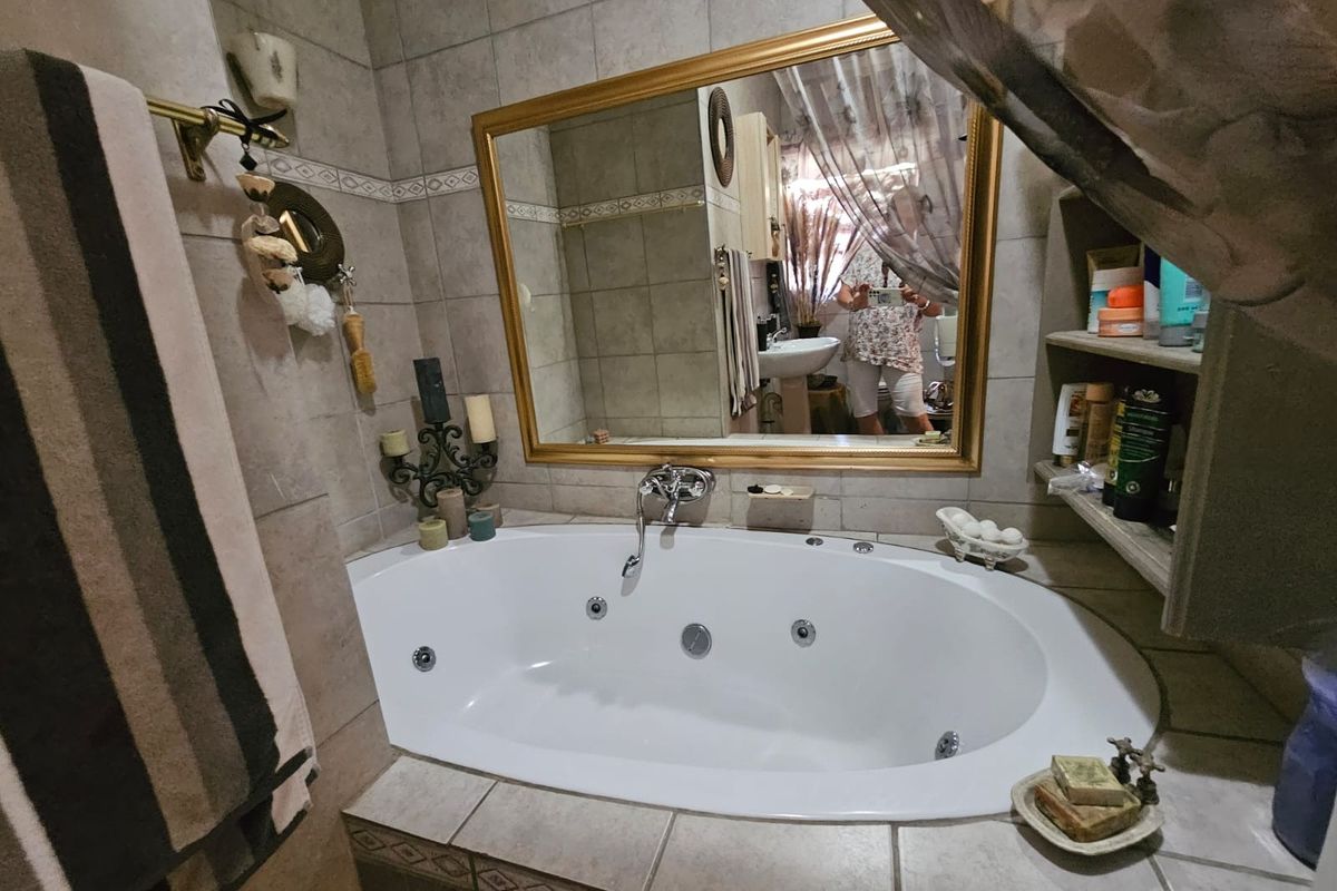A bathroom featuring a built-in jetted bathtub with tiled surround, wall-mounted faucet, and a large framed mirror.