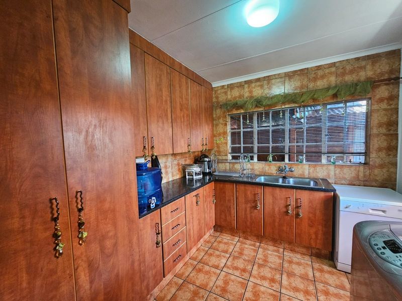 A functional kitchen featuring wood-look cabinetry, granite countertops, a double basin sink, and tiled finishes throughout.