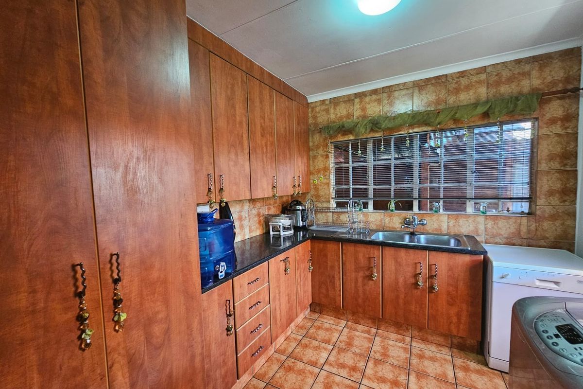 A functional kitchen featuring wood-look cabinetry, granite countertops, a double basin sink, and tiled finishes throughout.