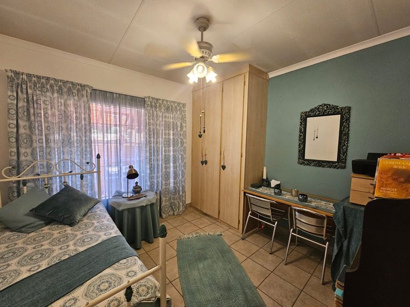 A functional bedroom featuring built-in cupboards, tiled flooring, and a ceiling fan, offering a comfortable and practical living space.