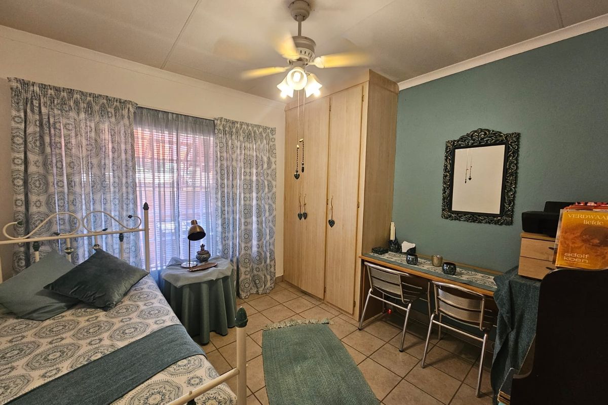 A functional bedroom featuring built-in cupboards, tiled flooring, and a ceiling fan, offering a comfortable and practical living space.