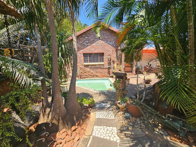 A private outdoor pool area featuring a brick-clad building exterior, paved patio space, and established garden surroundings.