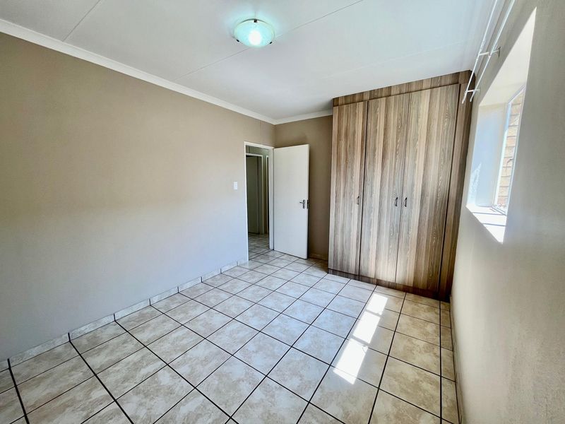 A bright, empty bedroom featuring neutral wall tones, tiled flooring, and a built-in wooden wardrobe, offering a clean canvas for personalization.