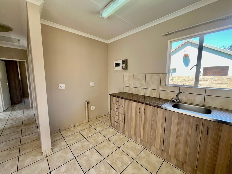 A clean and functional laundry room featuring laminate cabinetry, a stainless steel sink, tiled splashback, and ceramic floor tiles with dedicated plumbing connections.