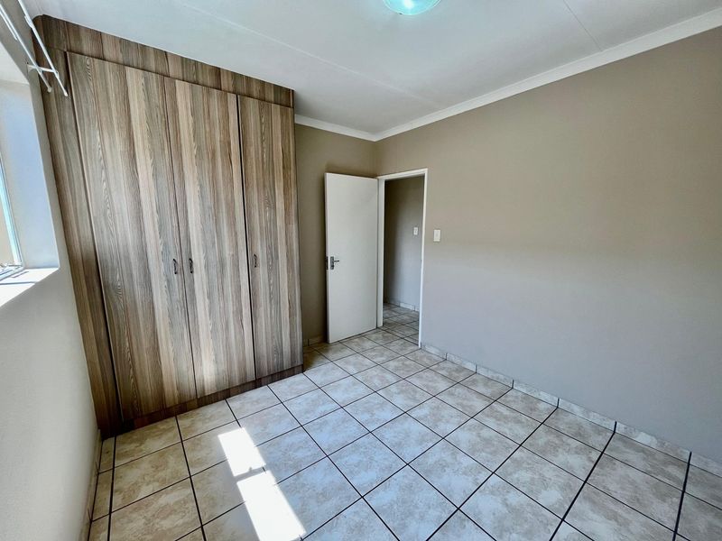 A clean, empty bedroom featuring neutral wall tones, durable tiled flooring, and ample built-in cupboard storage space.